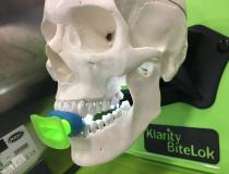 This is a new radiation oncology tongue immobilization device to prevent motion or variations in head or neck tumor positions during treatments. The Klarity BiteLok device is being displayed on the expo floor of the 2019 American Association of Physicists in Medicine (AAPM) meeting. It uses standard dental putty to mold to the patients mouth, and a clip to hold the mount in place as the head immobilization mask is molded. The mouth piece can be removed from the mask for cleaning.